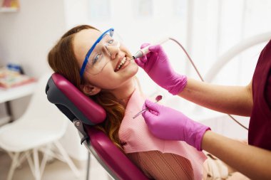 Koruyucu gözlüklü küçük kız klinikteki dişçiyi ziyaret ediyor. Stomatoloji kavramı.