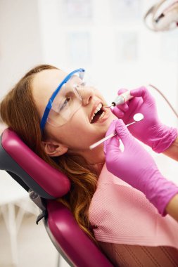 Koruyucu gözlüklü küçük kız klinikteki dişçiyi ziyaret ediyor. Stomatoloji kavramı.