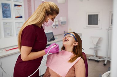 Koruyucu gözlüklü küçük kız klinikteki dişçiyi ziyaret ediyor. Stomatoloji kavramı.