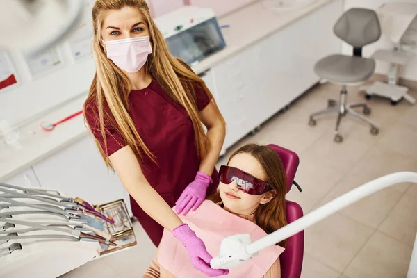 Koruyucu gözlüklü küçük kız klinikteki dişçiyi ziyaret ediyor. Stomatoloji kavramı.