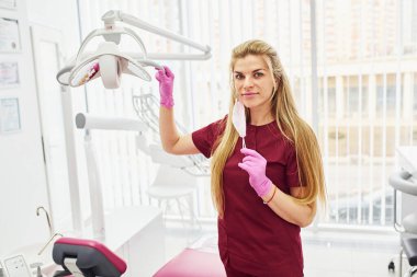 Üniformalı genç dişçi stomatoloji ofisinde duruyor..