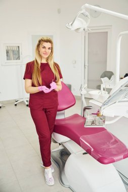 Üniformalı genç dişçi stomatoloji ofisinde duruyor..