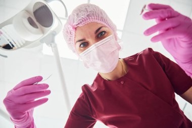 Young female dentist in protective mask working in stomatology clinic. First person view.