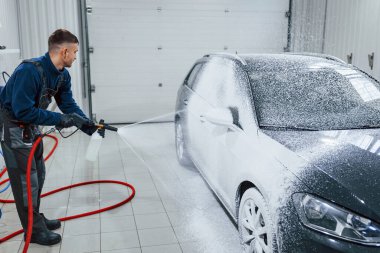 Üniformalı bir erkek işçi sabunla kaplanmış modern bir arabayı yıkıyor. Hizmet kavramı.