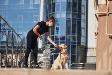 Koruyucu maskeli genç bir kadın karantina zamanında iş yerinin yakınında dışarıda yürüyüş yapıyor. Koronavirüs kavramı.