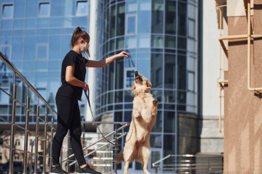 Koruyucu maskeli genç bir kadın karantina zamanında iş yerinin yakınında dışarıda yürüyüş yapıyor. Koronavirüs kavramı.