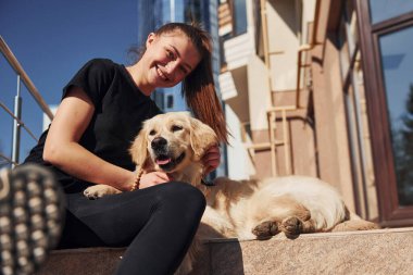 Birbirinize sarılın. Genç, pozitif bir kadın iş binasının yanında dışarıda dolaşırken köpeğiyle eğleniyor..
