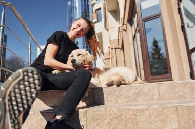 Birbirinize sarılın. Genç, pozitif bir kadın iş binasının yanında dışarıda dolaşırken köpeğiyle eğleniyor..