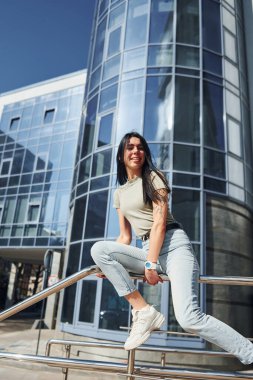 Kolunda dövmesi olan olumlu bir kadın güneşli bir günde iş binasına karşı dışarıda eğleniyor..