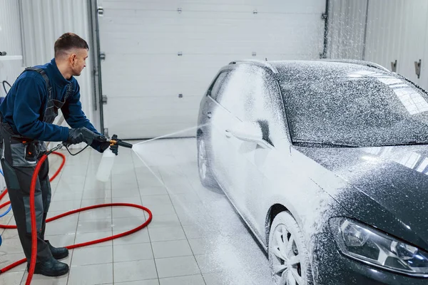 Üniformalı bir erkek işçi sabunla kaplanmış modern bir arabayı yıkıyor. Hizmet kavramı.
