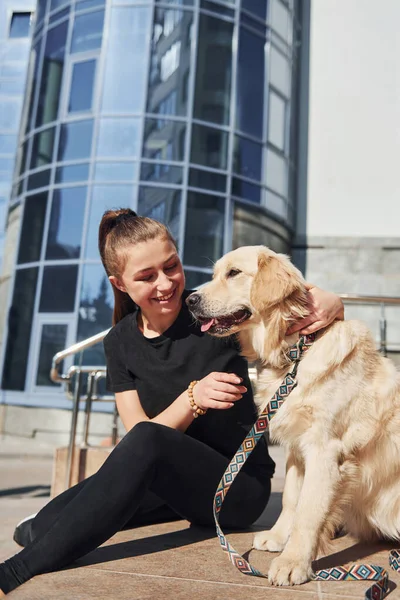 Genç, pozitif bir kadın iş binasının yanında dışarıda dolaşırken köpeğiyle eğleniyor..