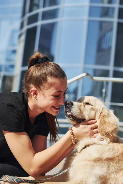 Genç, pozitif bir kadın iş binasının yanında dışarıda dolaşırken köpeğiyle eğleniyor..