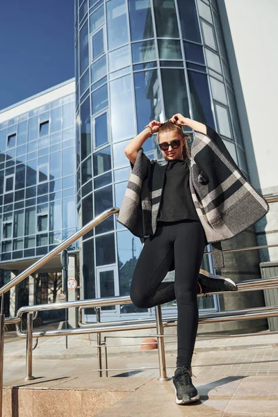 Young woman in sunglasses have walk outdoors near business building at sunny daytime.