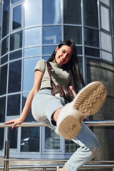 Kolunda dövmesi olan olumlu bir kadın güneşli bir günde iş binasına karşı dışarıda eğleniyor..