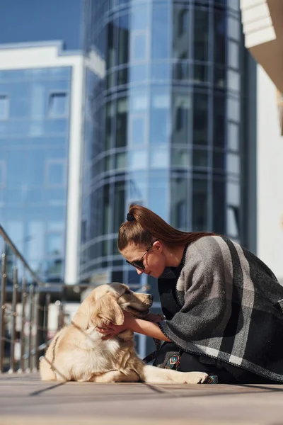 Genç, pozitif bir kadın iş binasının yanında dışarıda dolaşırken köpeğiyle eğleniyor..