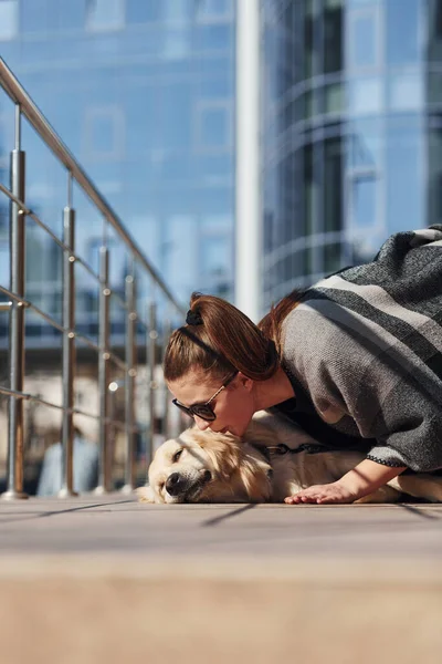 Genç, pozitif bir kadın iş binasının yanında dışarıda dolaşırken köpeğiyle eğleniyor..