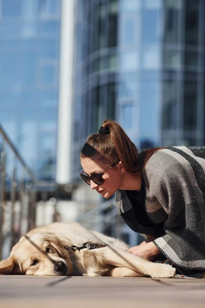 Genç, pozitif bir kadın iş binasının yanında dışarıda dolaşırken köpeğiyle eğleniyor..