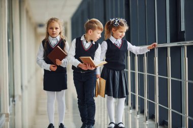 School kids in uniform together with books in corridor. Conception of education.