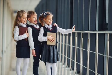 School kids in uniform together with phone and making selfie in corridor. Conception of education.