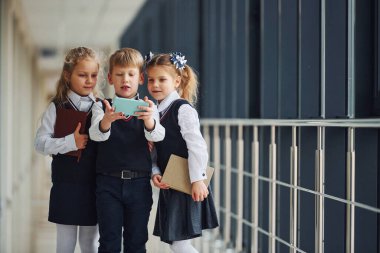 School kids in uniform together with phone and making selfie in corridor. Conception of education.