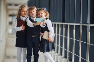 School kids in uniform together with phone and making selfie in corridor. Conception of education.