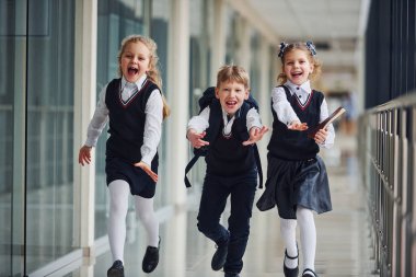 Active school kids in uniform running together in corridor. Conception of education.