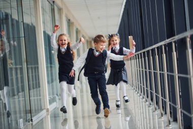 Active school kids in uniform running together in corridor. Conception of education.