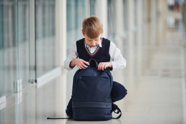 Okul üniformalı küçük çocuk koridorda sırt çantasıyla oturuyor..