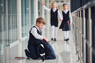 Boy sitting on the floor. School kids in uniform together in corridor.