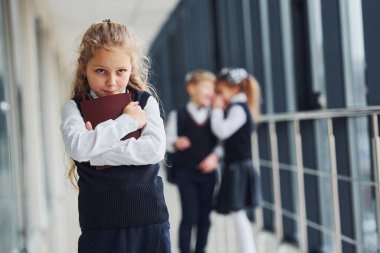Little girl gets bullied. Conception of harassment. School kids in uniform together in corridor.