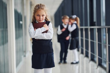 Little girl gets bullied. Conception of harassment. School kids in uniform together in corridor.