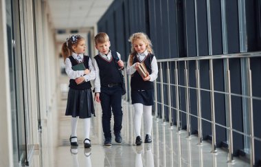 School kids in uniform with books together in corridor. Conception of education.
