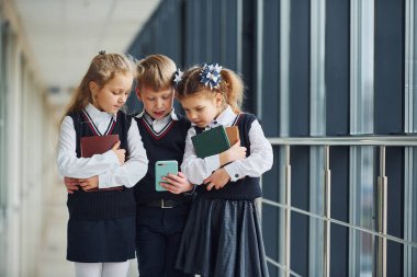 School kids in uniform together with phone in corridor. Conception of education.
