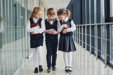 School kids in uniform together with phone in corridor. Conception of education.