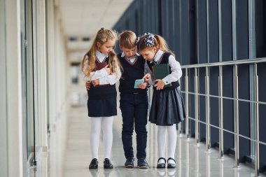 School kids in uniform together with phone in corridor. Conception of education.