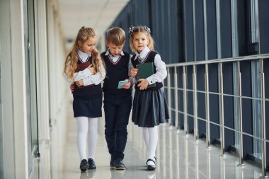 School kids in uniform together with phone in corridor. Conception of education.
