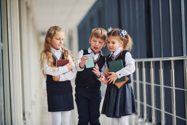 School kids in uniform together with phone in corridor. Conception of education.