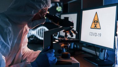 Laboratuvarda koronavirüsle çalışan beyaz koruyucu üniformalı bilim adamının yan görünüşü.