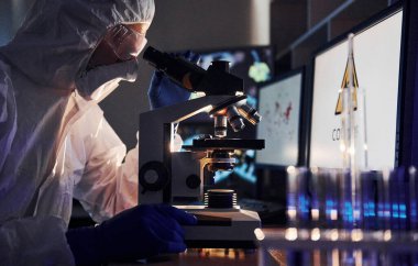 Laboratuvarda koronavirüsle çalışan beyaz koruyucu üniformalı bilim adamının yan görünüşü.