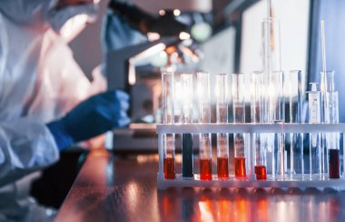 Scientist in white protective uniform works with coronavirus and blood tubes in laboratory.