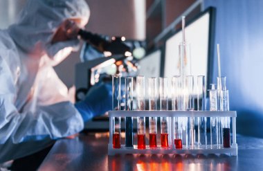 Scientist in white protective uniform works with coronavirus and blood tubes in laboratory.
