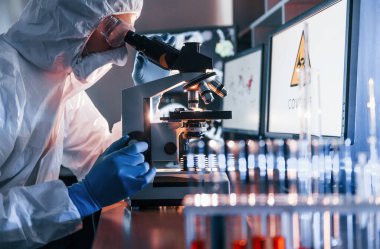 Beyaz koruyucu üniformalı bilim adamları laboratuarda koronavirüs ve kan tüpleriyle çalışıyorlar..
