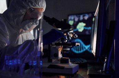 Laboratuvarda koronavirüsle çalışan beyaz koruyucu üniformalı bilim adamının yan görünüşü.