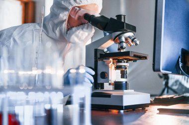 Masadaki bilgili monitörler. Beyaz koruyucu üniformalı bilim adamları laboratuarda koronavirüs ve kan tüpleriyle çalışıyorlar..