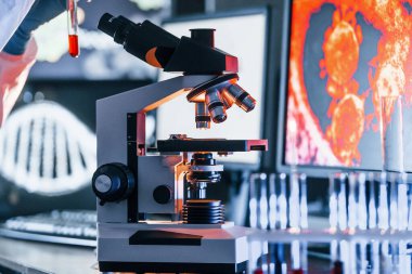 Masadaki bilgili monitörler. Beyaz koruyucu üniformalı bilim adamları laboratuarda koronavirüs ve kan tüpleriyle çalışıyorlar..