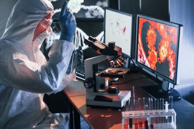Beyaz koruyucu üniforma giyen bilim adamları verilerle birlikte laboratuvarda koronavirüs ve kan tüpleriyle çalışıyorlar..