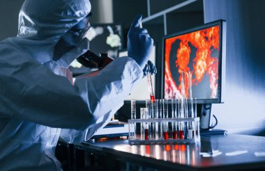 Beyaz koruyucu üniformalı bilim adamları laboratuarda koronavirüs ve kan tüpleriyle çalışıyorlar..