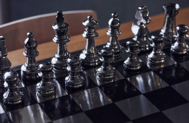 Üzerinde metal figürler olan satranç tahtası gündüz vakti masanın üstünde..