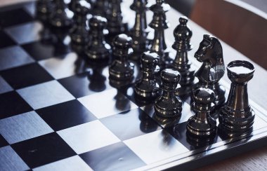 Üzerinde metal figürler olan satranç tahtası gündüz vakti masanın üstünde..