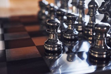 Üzerinde metal figürler olan satranç tahtası gündüz vakti masanın üstünde..